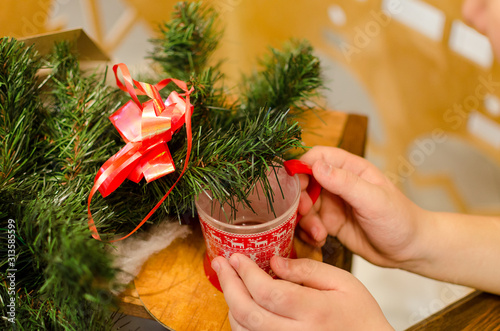 in the hands of Christmas red mug, room decorated for Christmas tree wreath. Classic interior in red and shades. Christmas at home. New Year decor