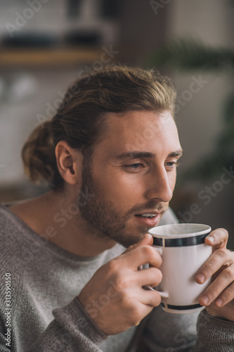 Young bearded handsome man in grey enjoying his coffee