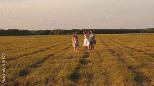 Children and mom are playing in the meadow. concept of a happy family. mother and little daughter with sisters walking in park. Happy young family with a child walking on summer field. © zoteva87
