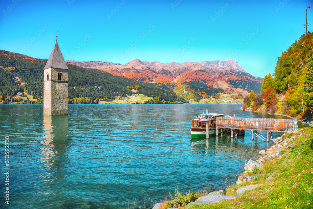 Fantastic autumn lake landscape with a ship near the pier and  submerged bell tower in lake Resia