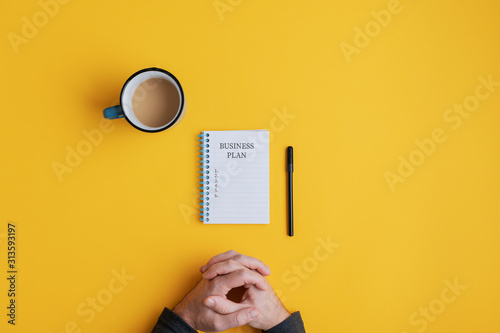 Man sitting by spiral notebook with Business plan ideas ready to be written in it