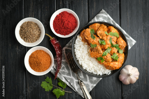 Chicken tikka masala traditional Asian spicy meat food with rice tomatoes and cilantro in a black bowl on dark wooden background.