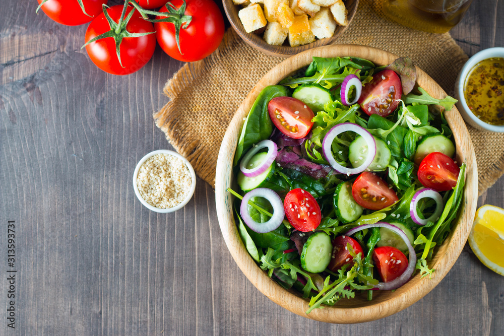 Fresh healthy salad with delicious ruccola, spinach, cabbage, arugula, feta cheese, red onion, cucumber, sesame seeds and cherry tomato on wooden background. Healthy and diet food concept. Fresh healthy salad with delicious ruccola, spinach, cabbage, arugula, feta cheese, red onion, cucumber, sesame seeds and cherry tomato on wooden background. Healthy and diet food concept.