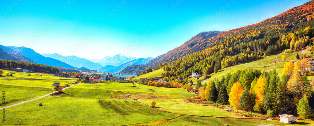 Magnificent autumn view of St.Valentin village and Haidersee (Lago della Muta) lake with Ortler peak on background.
