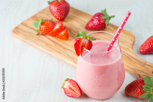 Glass of fresh strawberry milkshake, smoothie and fresh strawberries on pink, white and wooden background. Healthy food and drink concept.