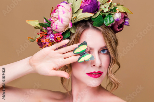 Young woman posing in flower wreath with artificial  greenbutterfly,  isolated on ochet background. One eye closed with a butterfly photo