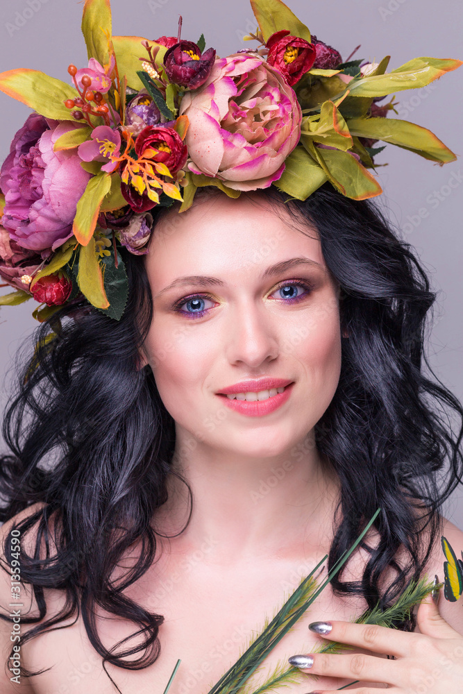 tender young brunette woman posing in flower wreath with artificial greenbutterfly, isolated on violet background tender young brunette woman posing in flower wreath with artificial greenbutterfly, isolated on violet background