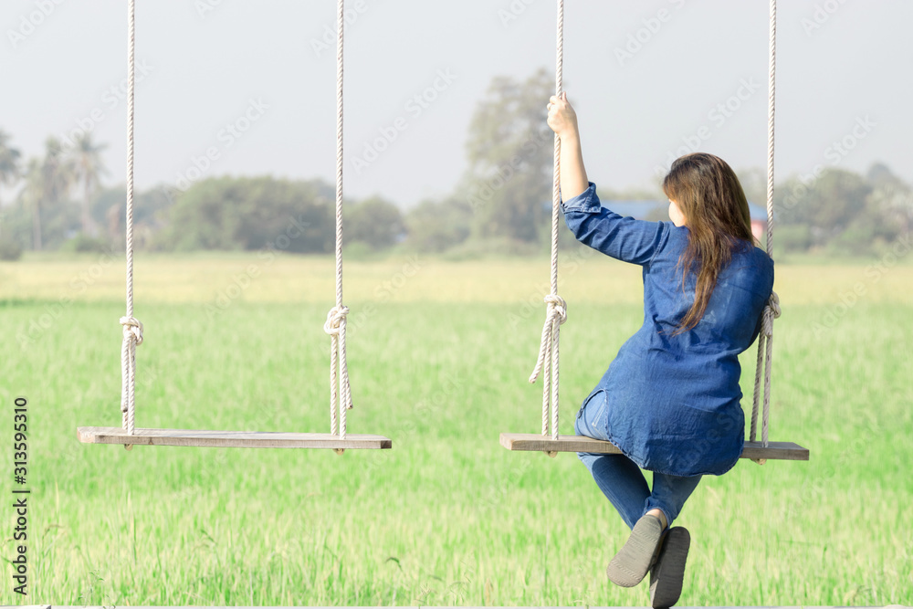 An Asian woman is happily sitting on a swing hanging among nature. On vacation An Asian woman is happily sitting on a swing hanging among nature. On vacation