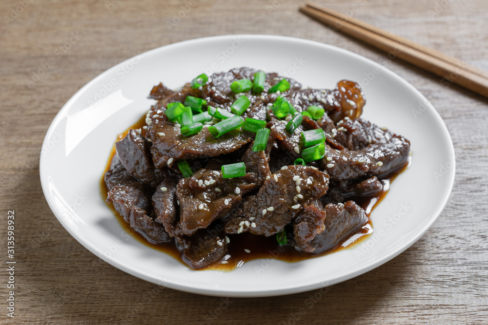 close up of stir fried beef with teriyaki sauce in a ceramic dish on wooden table. asian homemade style food concept.