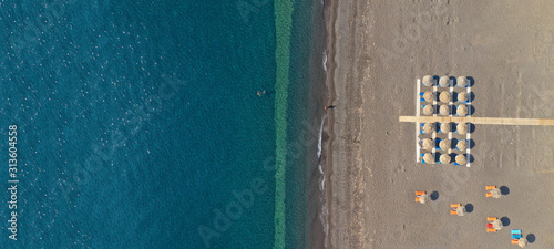 Aerial drone ultra wide top down photo of organised sandy beach in Kamari village, Santorini island, Cyclades, Greece