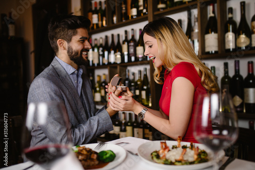 Handsome man proposing a beautiful woman to marry him in restaurant during date.