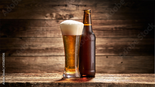 Szklanka pełna piwa i butelka na tle starych desek photo