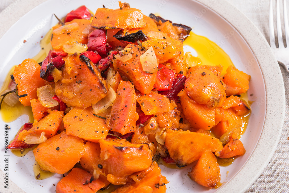 Tasty vegetarian dish - baked sweet potato with onions, carrots and spices in a plate on the table, close-up, rustic style Tasty vegetarian dish - baked sweet potato with onions, carrots and spices in a plate on the table, close-up, rustic style