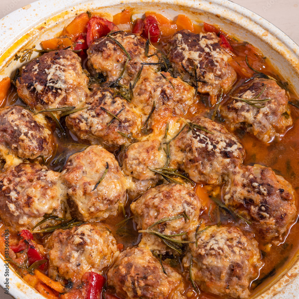 Tasty meatballs in homemade tomato sauce, baked with grated cheese and rosemary leaves in a large enameled pan, close-up, top view