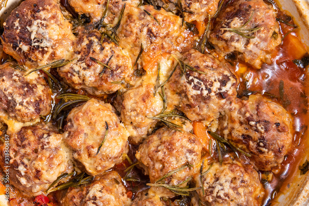 Tasty meatballs in homemade tomato sauce, baked with grated cheese and rosemary leaves, close-up, top view