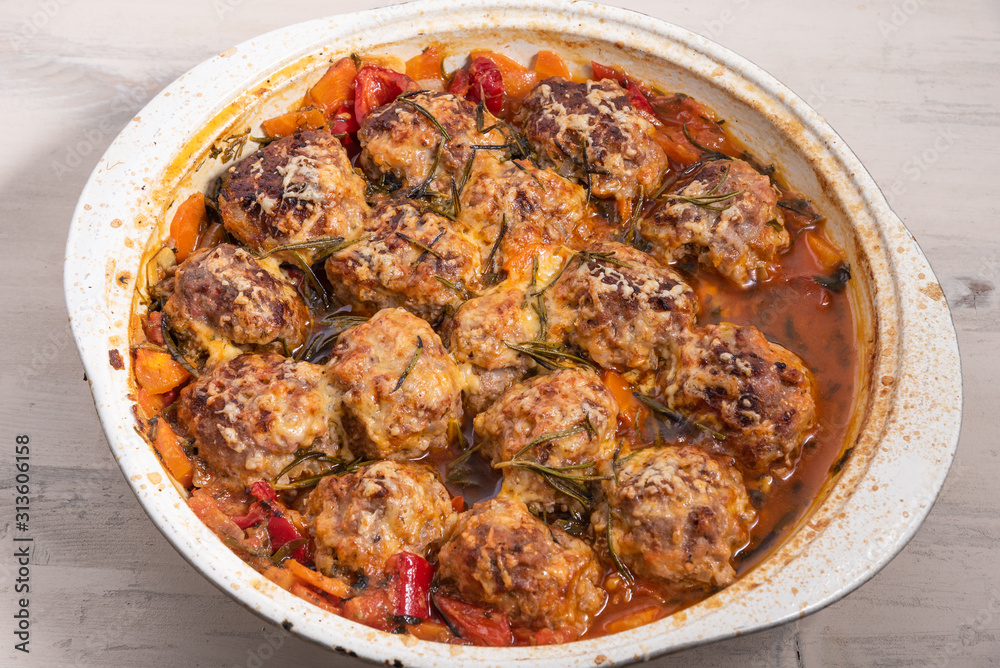 Tasty meatballs in homemade tomato sauce, baked with grated cheese and rosemary leaves in a large enameled pan, top view Tasty meatballs in homemade tomato sauce, baked with grated cheese and rosemary leaves in a large enameled pan, top view