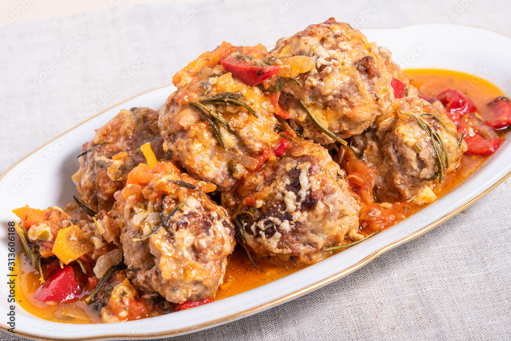 Delicious meatballs in homemade tomato sauce, baked with grated cheese and rosemary leaves on an oval dish Delicious meatballs in homemade tomato sauce, baked with grated cheese and rosemary leaves on an oval dish