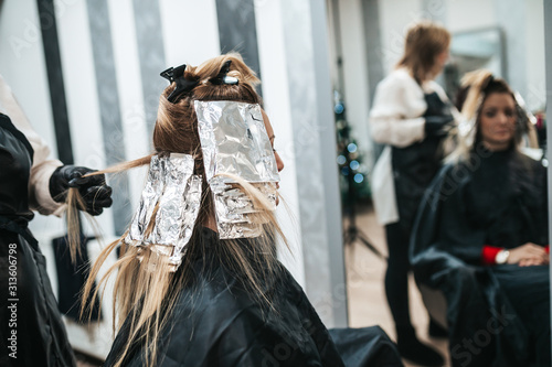 Hairdresser is dyeing female hair, making hair highlights to his client with a foil.