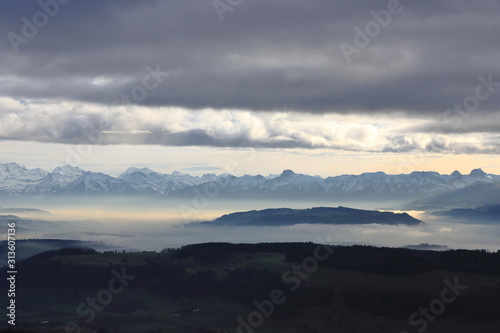Mountain of Belp surrounded by fog in front of Swiss alps panorama.