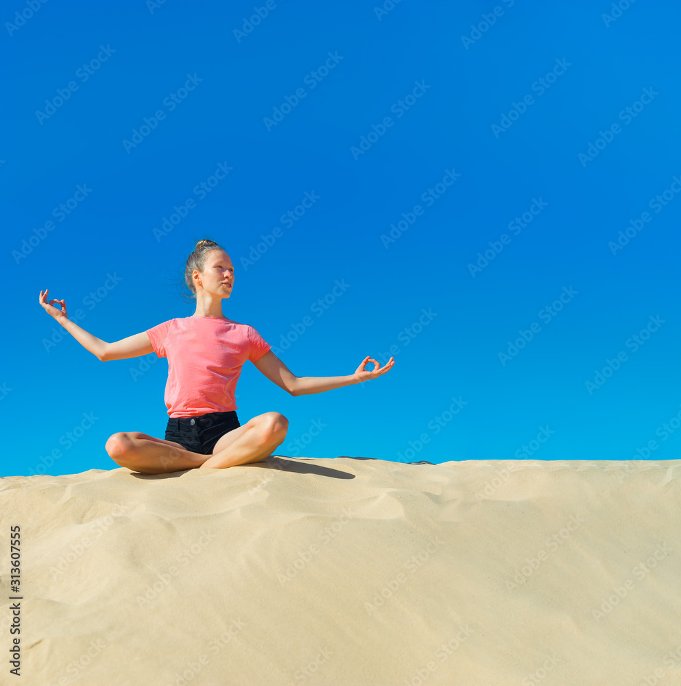 ein junges Mädchen macht im Sommer Yoga auf einer Düne im gelben Sand vor blauem Himmel ein junges Mädchen macht im Sommer Yoga auf einer Düne im gelben Sand vor blauem Himmel