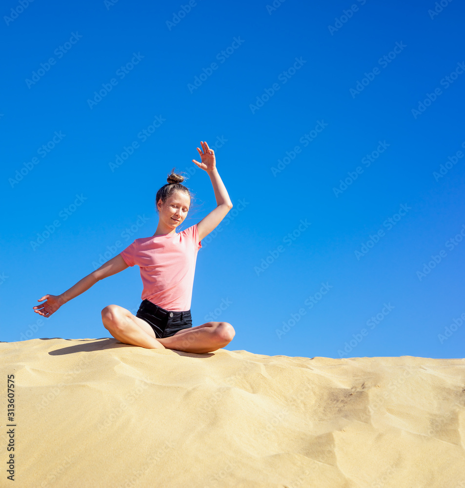ein junges Mädchen macht im Sommer Yoga auf einer Düne im gelben Sand vor blauem Himmel ein junges Mädchen macht im Sommer Yoga auf einer Düne im gelben Sand vor blauem Himmel
