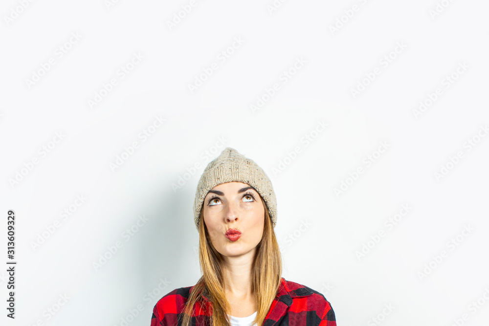 Young woman with a pensive face dreams of something in a hat, a red shirt and a white T-shirt on a white background. Stylish concept, dream, plan, goal, teenager style, shock, surprise. Banner Young woman with a pensive face dreams of something in a hat, a red shirt and a white T-shirt on a white background. Stylish concept, dream, plan, goal, teenager style, shock, surprise. Banner