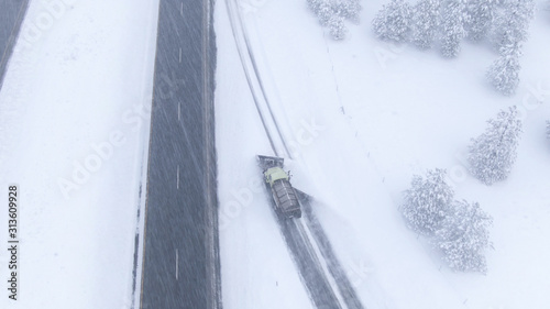 AERIAL: Snow ploughing truck clears and salts a highway lane during a snowstorm. © helivideo