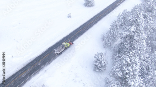 AERIAL: Snow ploughing truck cleans the country road leading through the forest.