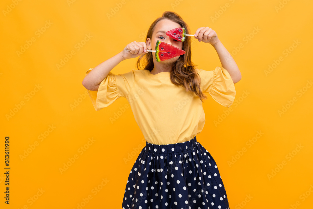 attractive caucasian young girl in a skirt and a t-shirt with two watermelon lollipops posing on a yellow background attractive caucasian young girl in a skirt and a t-shirt with two watermelon lollipops posing on a yellow background