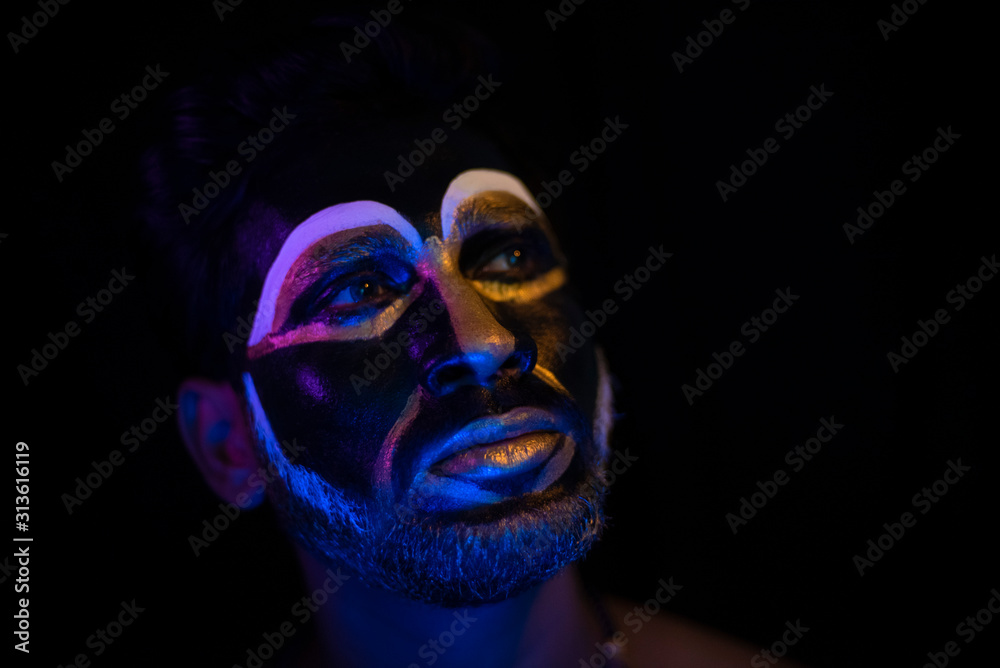 Close up of Indian brunette man with his face illuminated and painted by black and golden like a tribe standing with candle light in front of a black studio copy space background. Indian hi fashion. Close up of Indian brunette man with his face illuminated and painted by black and golden like a tribe standing with candle light in front of a black studio copy space background. Indian hi fashion.