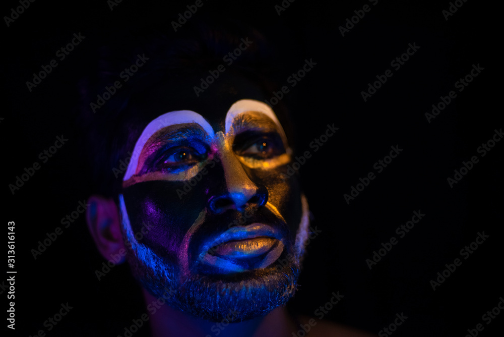 Close up of Indian brunette man with his face illuminated and painted by black and golden like a tribe standing with candle light in front of a black studio copy space background. Indian hi fashion. Close up of Indian brunette man with his face illuminated and painted by black and golden like a tribe standing with candle light in front of a black studio copy space background. Indian hi fashion.