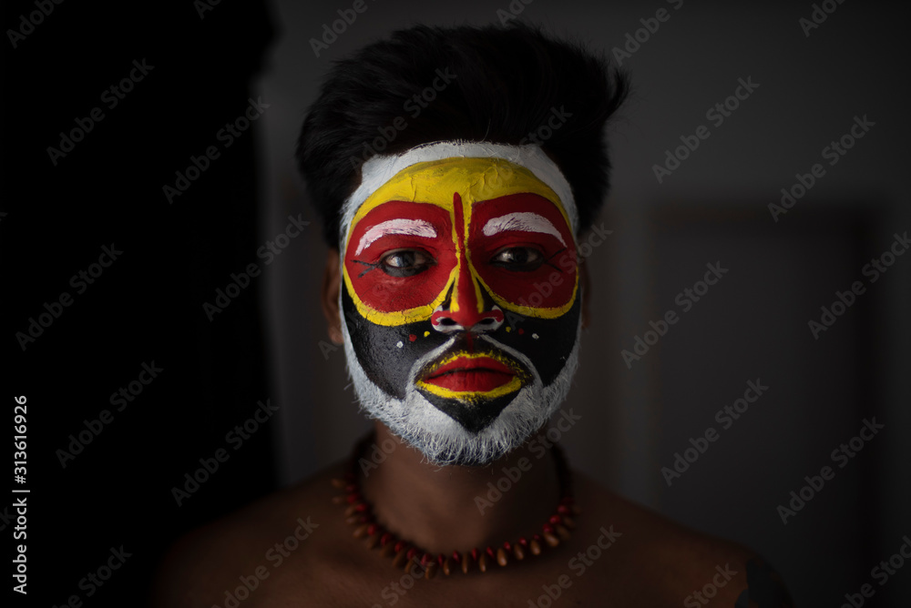 Close up portrait of an Indian brunette man with his face painted by vibrant colors like a tribe standing in front of a studio background. Indian hi fashion. Close up portrait of an Indian brunette man with his face painted by vibrant colors like a tribe standing in front of a studio background. Indian hi fashion.
