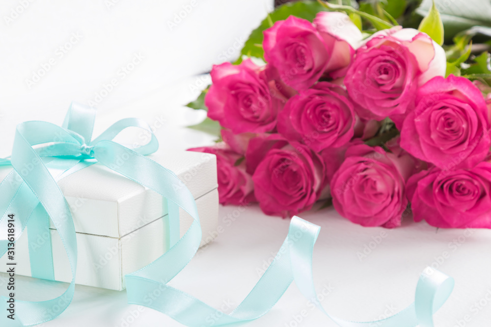 Gift box with turquoise ribbon and bouquet of pink roses on white background.