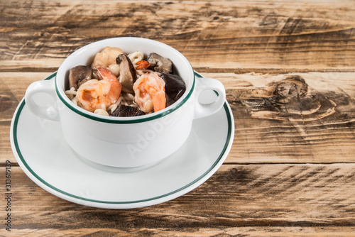 Chinese soup with udon noodles, pork, boiled eggs, mushrooms and prawns close-up in a bowl on the table photo