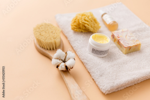 beauty, spa and wellness concept - close up of crafted soap bar, natural bristle wooden brush, body butter with sponge and essential oil on bath towel