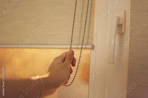 Foto Hand holds the chain and opens the roller blinds on the window, bed shade