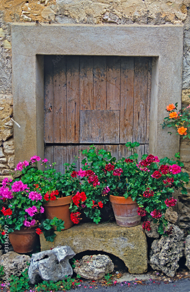 An old wooden door with surrounding stonework and planted geraniums  in Provence South of France