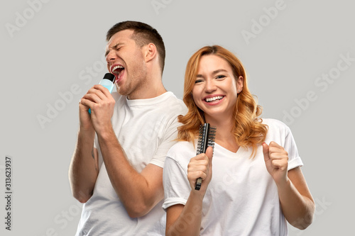relationships and people concept - portrait of happy couple in white t-shirts couple singing to hairbrush and lotion bottle over grey background