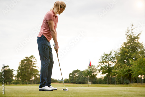 Rear View Of Female Golfer Putting Ball On Green