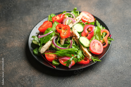 Fresh vegetable salad with chicken meat, herbs and olive oil in a dark plate on a dark background. Healthy food. Top view copy space.