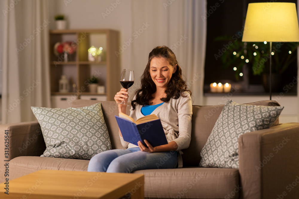 leisure, literature and people concept - young woman reading book and drinking red wine at home in evening leisure, literature and people concept - young woman reading book and drinking red wine at home in evening