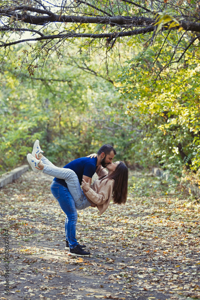 Young beautiful couple in the Park. A man holds a woman in his arms. In the background autumn forest.