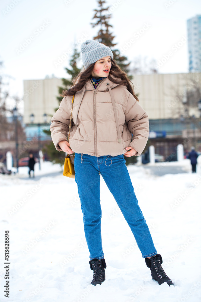 Portrait of young girl in blue jeans walking in a winter park
