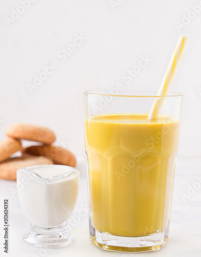 healthy latte with turmeric and spices on a white plate next to milk and cookies. golden milk