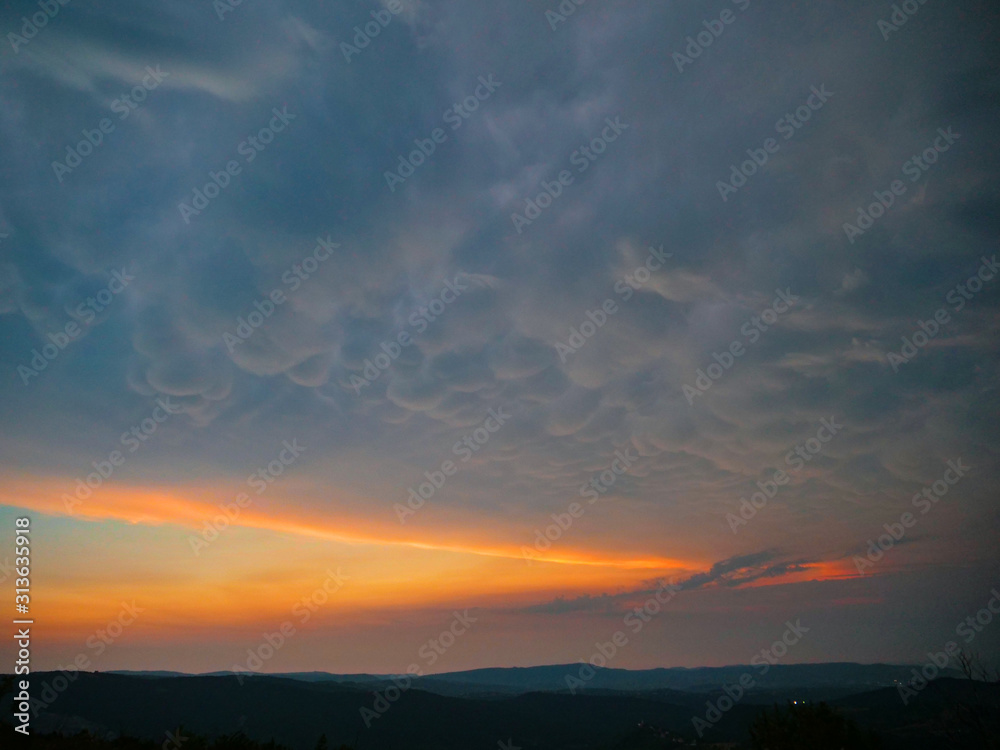 Dark mammatus clouds gather above the peaceful countryside at golden sunset.