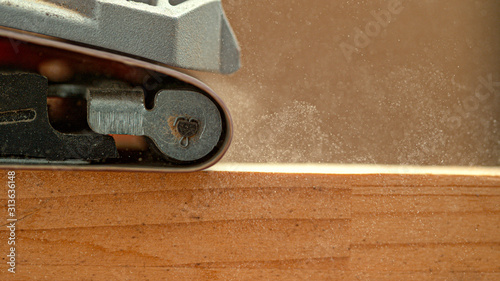 Fotografie MACRO: Sanding machine smooths out wooden board sitting on carpenter's workbench