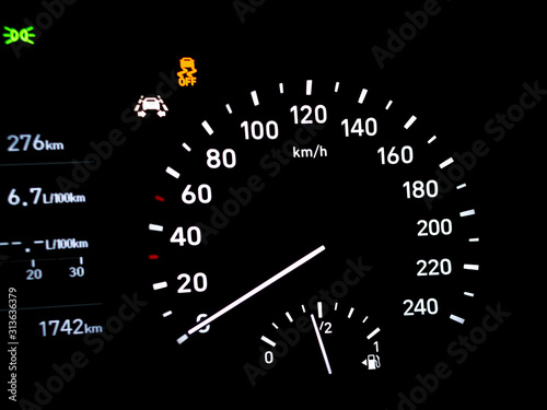 Side view of modern car dashboard with circular speedometer, fuel gauge indicator, odometer, traction control (ASR) and parking lights icon. Close up of petrol level showing on car instrument panel.