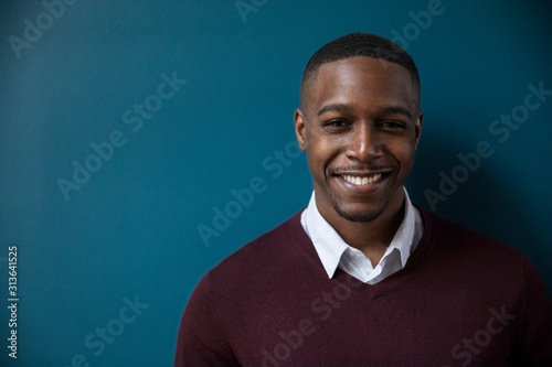 Portrait of confident smiling businessman standing against wall in darkroom at office