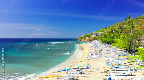Drone moving forward over the white fisherman boats on the sand at Amed beach, surrounded by majestic green palms tree in Bali, Indonesia. Aerial view 4K photo