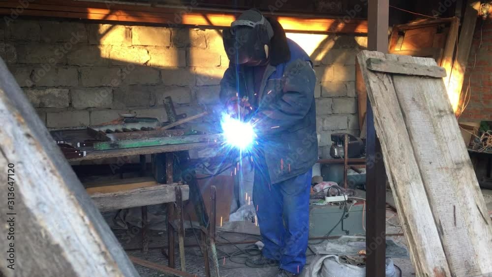 man welds a metal welding machine in the street a grey wall on the background, there are a lot of tools on the table for work man welds a metal welding machine in the street a grey wall on the background, there are a lot of tools on the table for work
